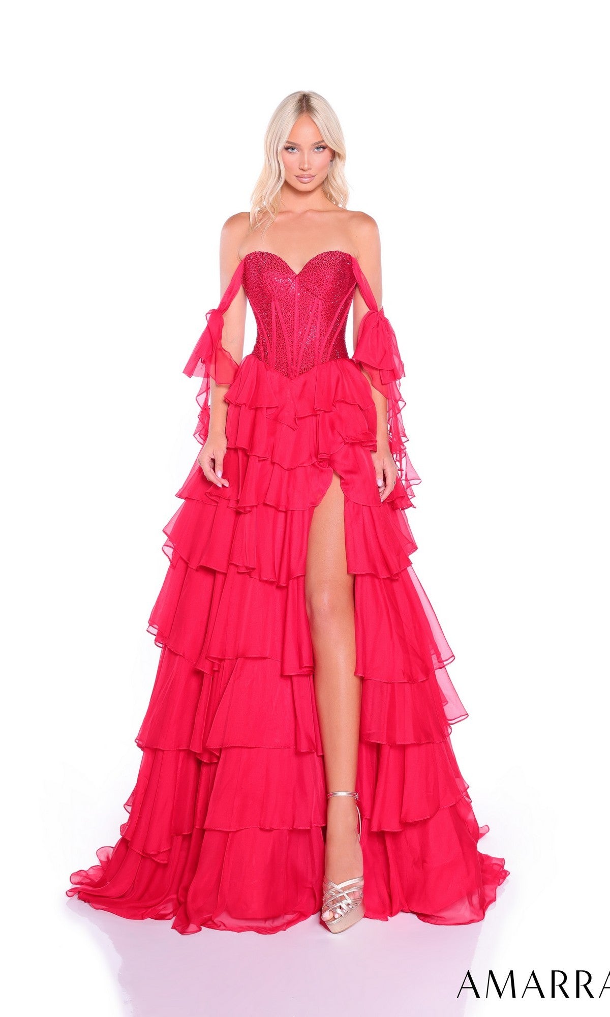 A woman wears the Amarra 89285 long prom dress, featuring a bright pink, strapless bodice with a tiered chiffon skirt and high slit, standing against a white background.